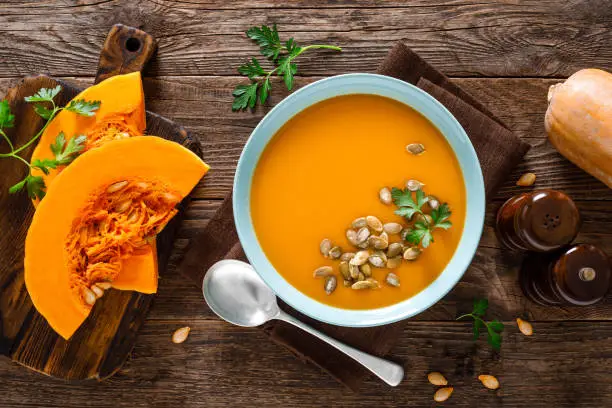 Photo of Pumpkin soup. Vegetarian soup with pumpkin seeds in bowl on wooden table, top view