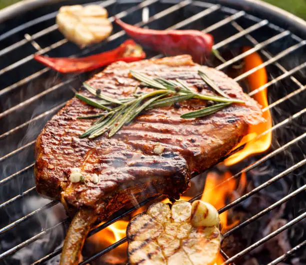 Photo of Grilled bone-in pork chop, pork steak, tomahawk in spicy marinade on a flaming grill flat, close-up.