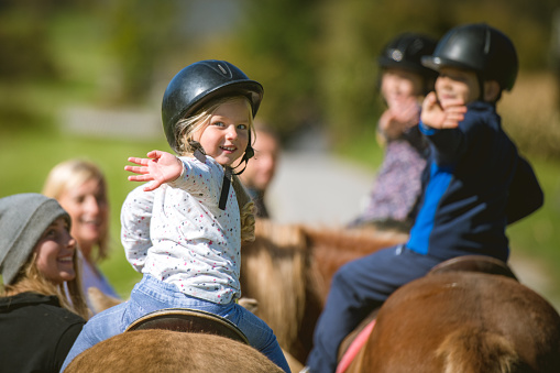 Children training horseback riding with the help of their parents on ranch.