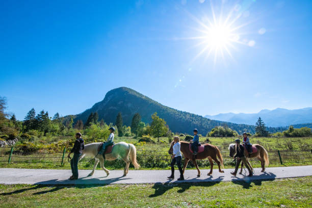 Children training horseback riding with the help of their parents on ranch.