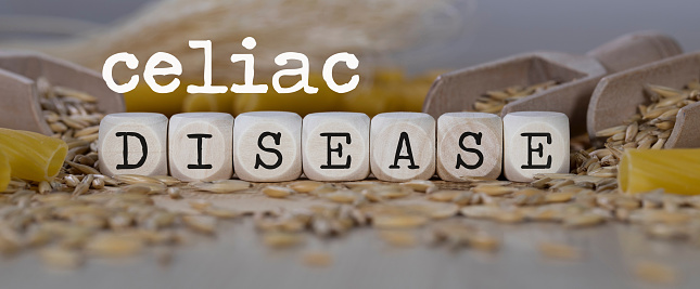 Words CELIAC DISEASE  composed of wooden dices. Rye grains in the background. Closeup