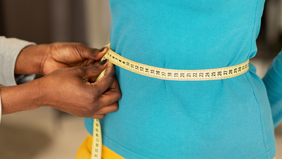 Design Studio Concept. African American Female Hands Measuring Slim Woman's Waist With Yellow Tape. Closeup, Panorama