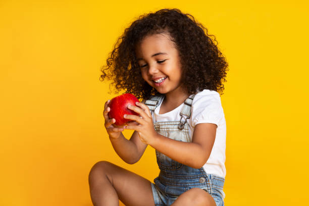 bonita chica sosteniendo manzana roja sobre fondo de estudio amarillo - child food fruit childhood fotografías e imágenes de stock