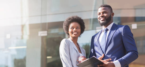 Couple of business partners standing against modern glass building background Couple of african business partners standing against modern glass building background, panorama with copy space african american business couple stock pictures, royalty-free photos & images