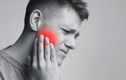 Dental problem. Young man suffering from strong toothache, monochrome photo with red inflamed zone, free space