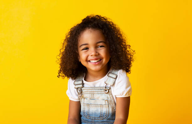 Happy smiling african-american child girl, yellow background Happy african-american child girl smiling to camera over yellow background curly hair stock pictures, royalty-free photos & images