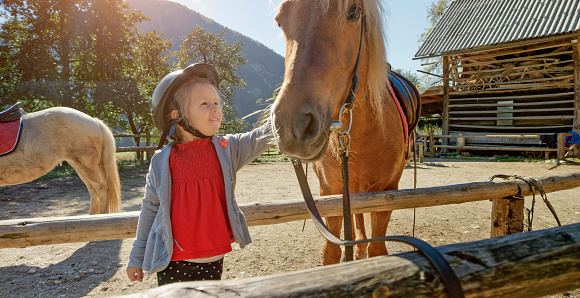 Smiling little girl touching horse on ranch.