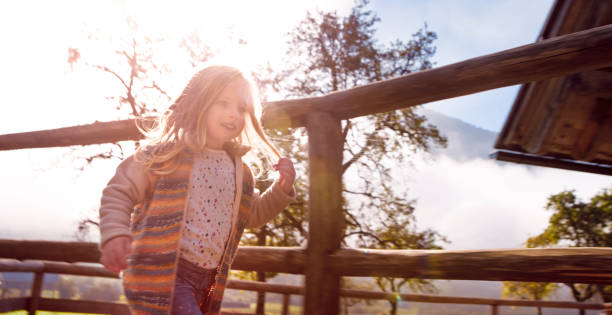 Blurred motion of smiling little girl running on ranch by fence.
