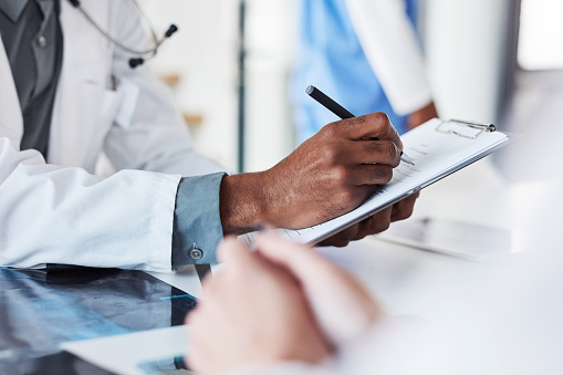 Closeup shot of an unrecognisable doctor writing on a clipboard in an hospital