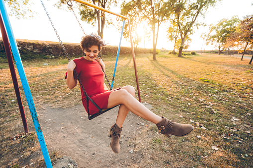 Young beautiful caucasian  woman on a swing in a park on beautiful sunny autumn day.