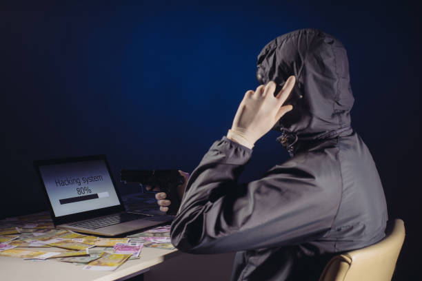 istock Anonymous hacker programmer uses a laptop holding a gun in his hand to hack the system in the dark. Creation and infection of malicious virus. 1168387061