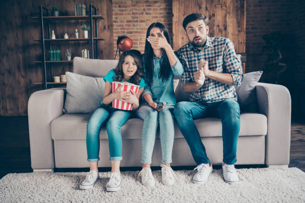 portrait of shocked people with wavy curly long hair sit divan watch tv wearing plaid shirt denim jeans in house indoors - remote television movie box imagens e fotografias de stock