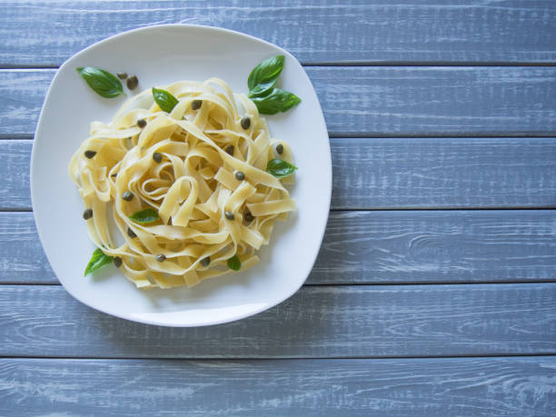 istock Fettuccine served on white plate with basil and capers on light grey wooden background. Selective focus, copy space 1168399772