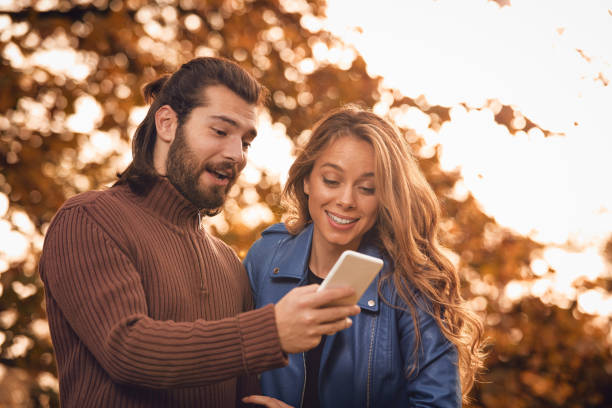 istock Young couple using cellphone in autumn colored park. 1168405198