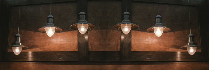 Glowing retro lamps hang on a brown wooden background. Retro background.