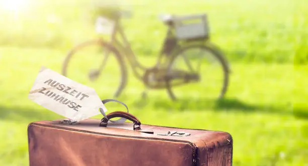 Old leatrher suitcase in the garden with bicycle with sign time out at home "Auszeit Zuhause"