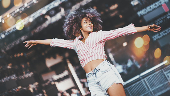 Young african american woman jumping in front of the stage at music festival.