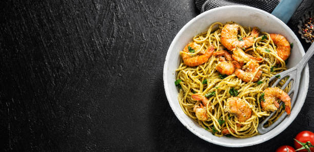 Spaghetti pasta with pesto and shrimps Tasty appetizing pasta spaghetti with pesto sauce and shrimps served on pan on dark background. Top View with Copy Space. Banner food state preparation shrimp prepared shrimp stock pictures, royalty-free photos & images