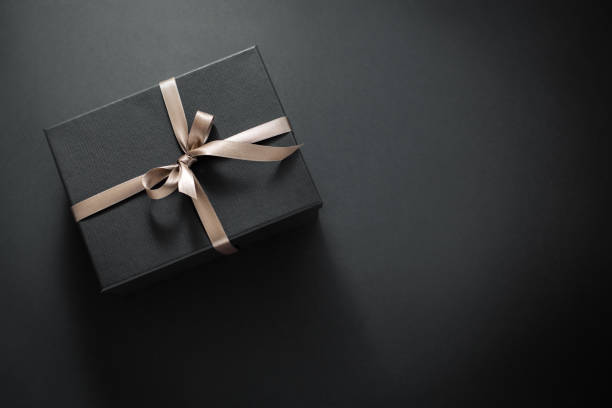 Gift wrapped in dark paper on dark background One gift wrapped in dark black paper with luxury bow on dark background. Horizontal with copy space. gift pack stock pictures, royalty-free photos & images