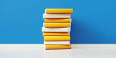istock Colorful Books Sitting On Top Of Each Other In Front of Blue Wall 1168415132