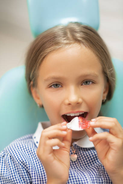 Close up of beautiful schoolgirl holding mouth guard Mouth guard. Close up of beautiful schoolgirl holding mouth guard while sitting in dental chair sequence dress stock pictures, royalty-free photos & images