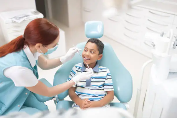 Dentist examining cavity. Dark-eyed handsome cute boy opening mouth while dentist examining cavity
