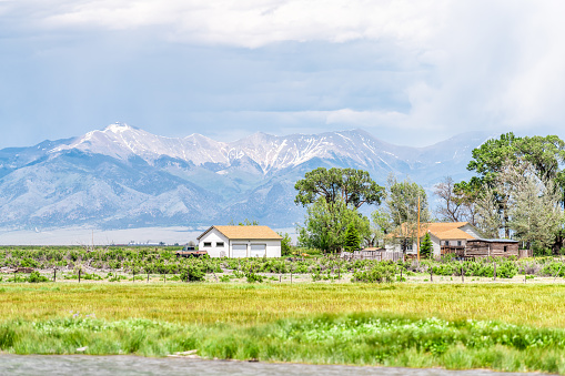 Center, USA - June 20, 2019: Colorado route road 285 with rural farm pasture and wooden house near Monte Vista and view of Rocky Mountains