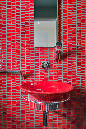 in the foreground the red ceramic washbasin suspended with red mosaic coating in the modern bathroom