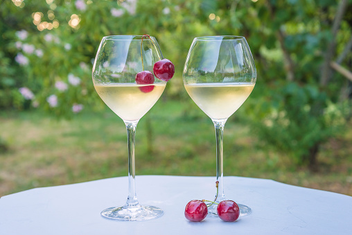 Two glass of cold white wine and red cherries on the white table in the garden