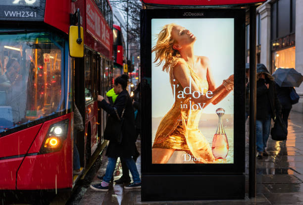 Boarding a London Bus and bus stop advertising London, UK - People boarding a double decker bus in central London, at a bus stop with a digital advertising display showing an advertisement for a Dior fragrance. bus shelter stock pictures, royalty-free photos & images