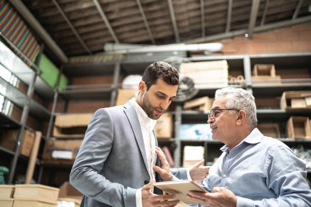 istock Senior and young business owner checking products in a storage room, using digital tablet 1168440932