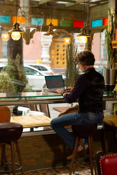 Focused on work. Serious adult man sitting at the cafe near the window table working on his laptop and drinking coffee.