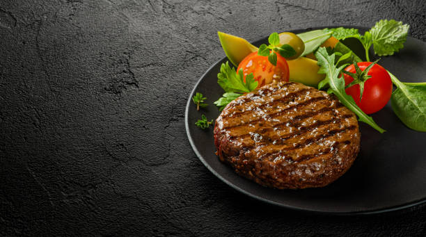 Juicy grilled burger cutlet with salad leaves on dark table