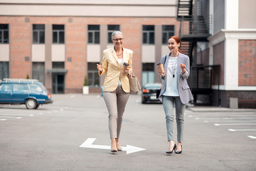 Two smiling ladies. Two stylish smiling ladies with paper cups of coffee smiling while walking together outdoors
