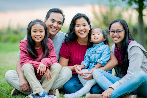 Filipino family portrait outside in the summertime A family smiles as they sit together on the grass. They have beautiful, genuine smiles, except for the cute toddler girl who looks tired. big family sunset stock pictures, royalty-free photos & images