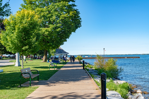 Tourists walking along the plank road by the lake.\nDuring summer weekend, many family come to Couchiching Beach Park to swim in Orillia Ontario, Canada.