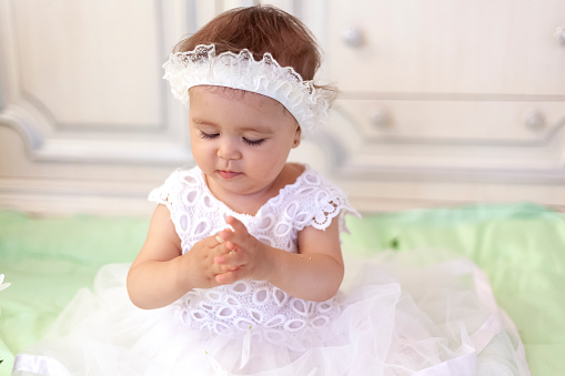 Baby girl in white dress taking a beautiful single white flower. Little princess playing with a white flower at her first birthday