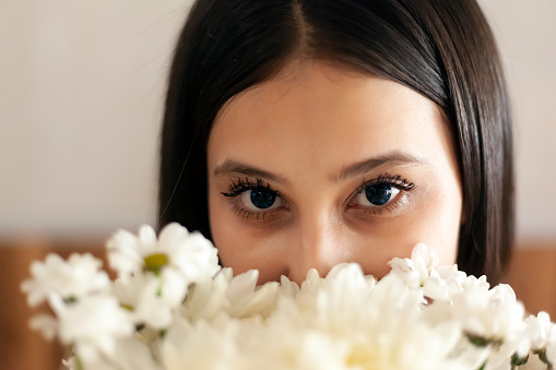 Attractive middle-eastern girl with beautiful eyes looking into the camera from behind flowers bouquet. Close-up view of young charming female.