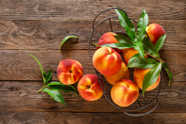 istock Ripe peaches with leaves in basket on wooden table, top view 1168452111