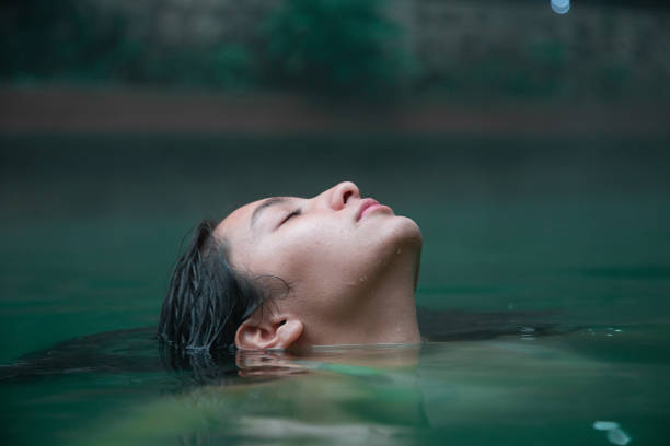 mujer viajera disfrutando de un día de spa en aguas termales naturales - mujer joven hispana sumergida hasta su cara en el agua con los ojos cerrados - baños térmicos fotografías e imágenes de stock