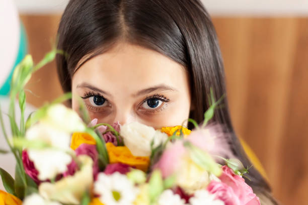 istock Attractive middle-eastern girl with beautiful eyes looking into the camera from behind flowers bouquet 1168453710