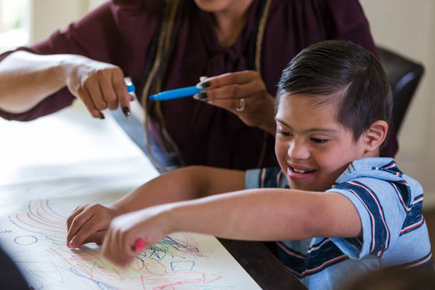 istock Young boy with Down Syndrome enjoys coloring with unrecognizable therapist 1168467221