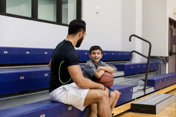 sentado en las gradas, papá da consejos de hijo pequeño sobre baloncesto - sport parent bleachers family fotografías e imágenes de stock
