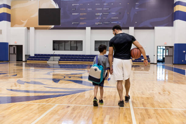 Father and son walk away from basketball court after game An unrecognizable father and son walk away from the basketball court in the school gym after the game. youth basketball indoor stock pictures, royalty-free photos & images