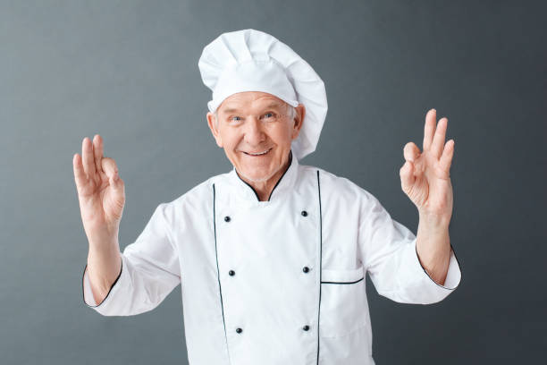 istock Senior chef studio standing isolated on gray showing ok gesture looking camera positive 1168473822