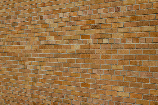 This vintage grungy brick wall abstract background has orange brown color bricks in a common bond pattern with a somewhat worn industrial look. (angle view)