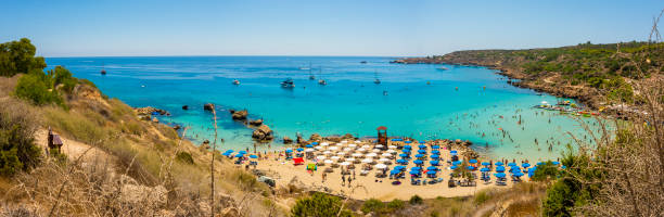 mare blu con acqua limpida, montagne, yacht e la spiaggia sul panorama della baia di konnos cipro - clear sky panoramic grass scenics foto e immagini stock