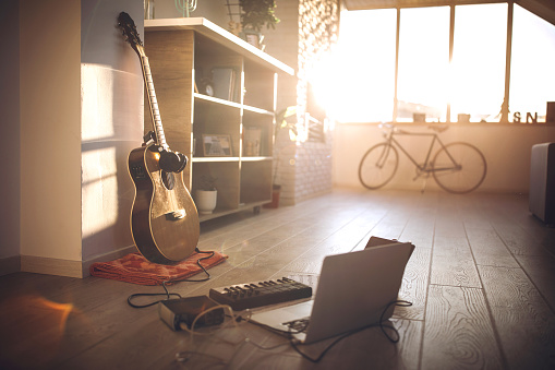 Guitar on floor at apartment, near laptop and mixing music equipment, on sunny day