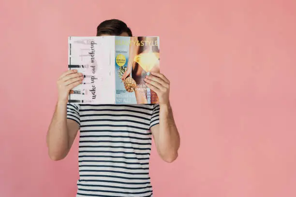 Photo of front view of man in striped t-shirt reading magazine isolated on pink