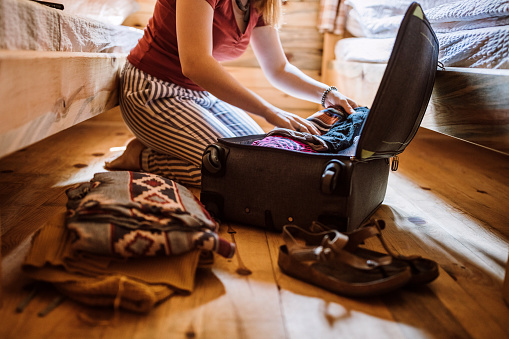 Unrecognizable woman packing luggage in log cabin, sitting on floor